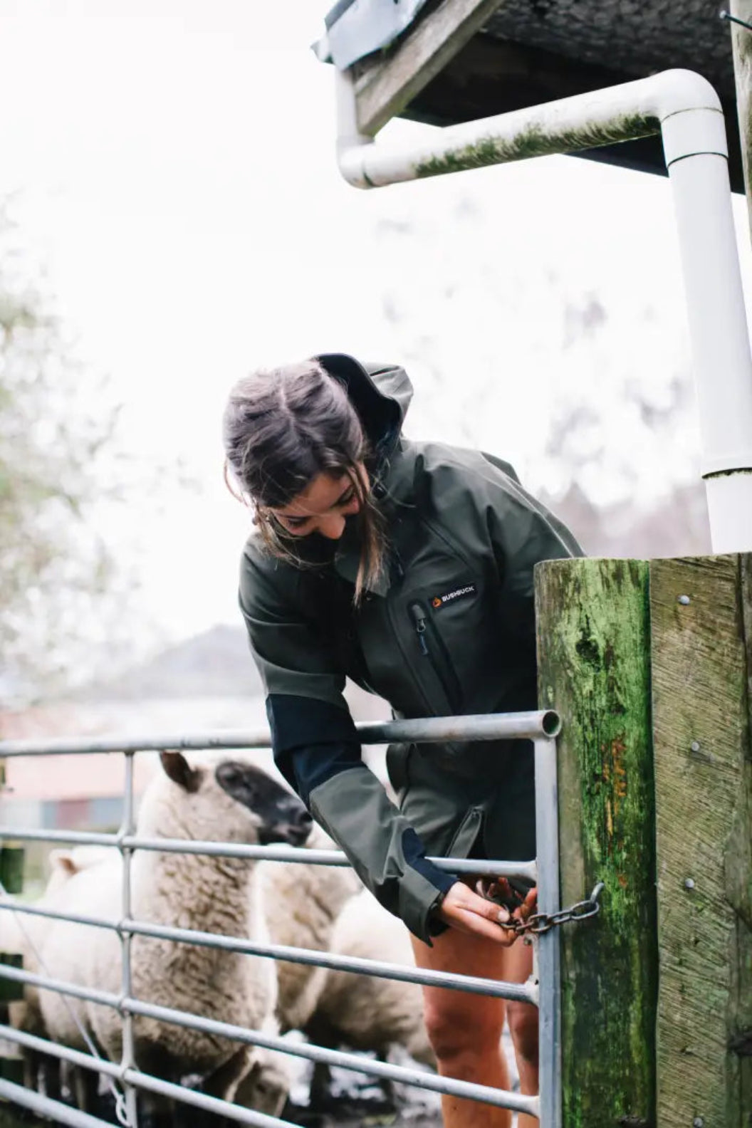 Woman in green Bushbuck Defender Waterproof Jacket opening sheep pen gate for country clothing and hunting stuff
