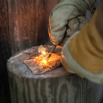 Gloved hands using Kupilka Firesteel as a compact striker to ignite wood