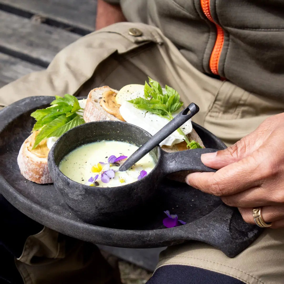 Rustic black Kupilka Plate with soup and sandwiches on a cozy country table